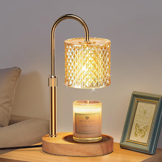Um candeeiro aquecedor de velas elegante com estrutura dourada e cúpula de cristal âmbar, iluminando uma vela perfumada sobre uma base de madeira numa mesa de cabeceira.