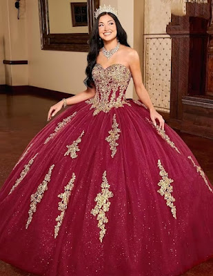 Uma imagem cativante de uma jovem deslumbrante vestindo um opulento vestido de Quinceañera. O vestido, em um rico tom borgonha, apresenta um corpete sem alças coberto por intrincados bordados dourados. A saia de baile volumosa é feita de camadas de tule brilhante e é acentuada por apliques dourados verticais que descem em cascata. Ela usa uma coroa de cristal cintilante e joias de declaração, incluindo um colar e brincos reluzentes. Seu cabelo escuro e ondulado flui pelas costas enquanto ela sorri radiantemente, irradiando confiança e alegria em um ambiente elegante de salão de festas.