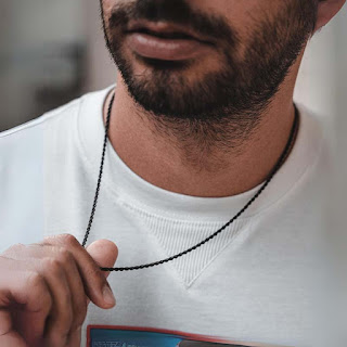 Homem com barba a usar colar masculino preto minimalista, combinado com t-shirt branca Colar masculino preto minimalista em detalhe