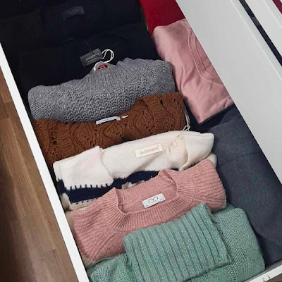 Gaveta de closet com camisolas de outono enroladas e organizadas por cores, mostrando um método de arrumação que permite ver todas as peças facilmente.