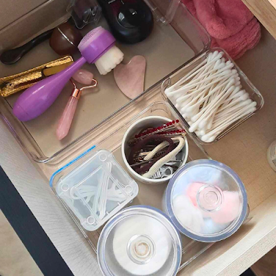 Gaveta com acessórios e produtos de beleza organizados em caixas transparentes: discos de algodão, cotonetes, ganchos, esponjas e ferramentas de skincare.