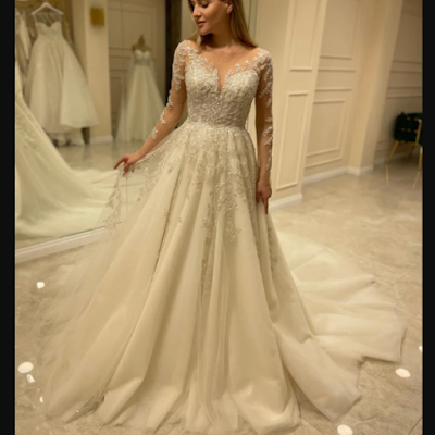 Noiva a experimentar vestido de noiva romântico, com mangas compridas em renda, decote em V e saia fluida em tule, num atelier de noivas