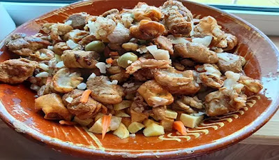 Comida de conforto: a tradição dos Rojões Prato de barro tradicional português servido com uma generosa porção de rojões de carne de porco dourados, acompanhados por cubos de batata frita, tripa enfarinhada, redenho, azeitonas e tiras de cenoura.