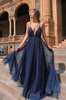 Mulher com vestido longo azul-marinho de lantejoulas e alças finas, com decote profundo e saia esvoaçante, ideal para festas formais ou eventos noturnos ao ar livre.
