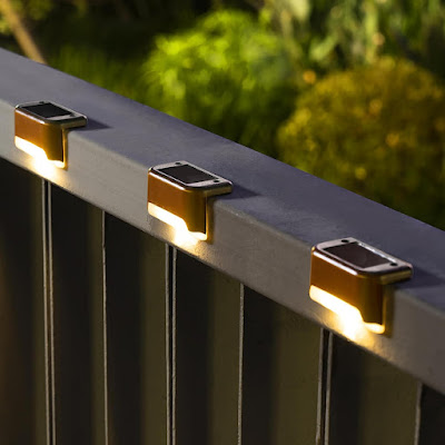 Iluminação Estratégica: O Charme das Luzes Solares Close-up de três pequenas luzes solares instaladas no topo de um corrimão metálico à noite. As luzes emitem um brilho quente e suave, criando um efeito de iluminação elegante e acolhedor para espaços exteriores, como terraços ou varandas.