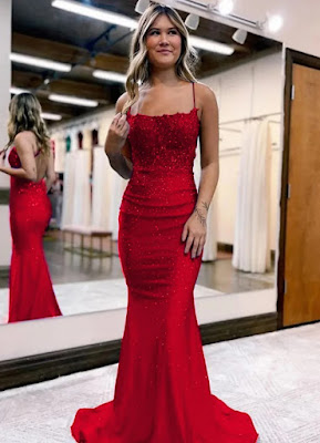 A young woman in a red mermaid sequin prom dress posing in a boutique setting with mirrors and dresses in the background.