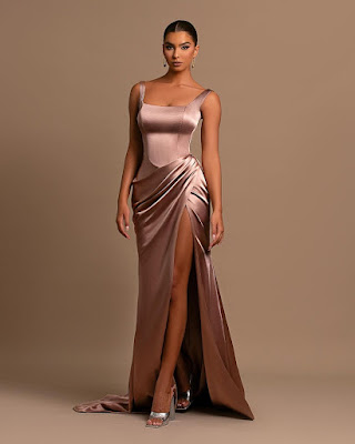 Mulher elegante com vestido split dress acetinado cor bronze, com abertura lateral profunda, decote quadrado e cauda, combinando com sandálias prateadas de salto.