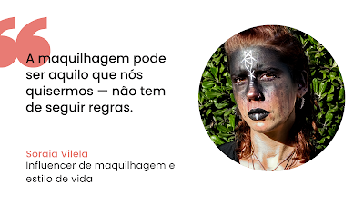 Grafismo digital de citação sobre fundo branco. À esquerda, aspas grandes em coral precedem o texto preto: "A maquilhagem pode ser aquilo que nós quisermos — não tem de seguir regras." Abaixo, o nome "Soraia Vilela" em coral e a sua ocupação "Influencer de maquilhagem e estilo de vida" em preto. À direita, um retrato fotográfico circular de Soraia Vilela, que tem cabelo ruivo, apresentando uma maquilhagem artística e dramática: o rosto está pintado com pigmento preto mate cobrindo a testa e os olhos, com um símbolo branco geométrico no centro da testa e linhas brancas nos lábios também pintados de preto. O fundo da foto mostra folhagem verde ao ar livre sob luz solar direta.