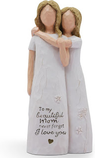 Estatueta de resina pintada à mão representando uma mãe e filha abraçadas, ambas com vestidos brancos e sem traços faciais definidos. Na base, lê-se a mensagem carinhosa: "To my beautiful Mom never forget I love you" (Para a minha linda mãe, nunca esqueças que te amo).