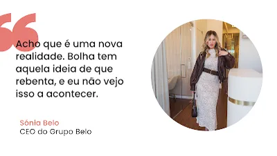 Citação de Sónia Belo sobre o Mercado Imobiliário Imagem com fundo branco dividida em duas partes. Do lado esquerdo, destaca-se um símbolo de aspas cor-de-rosa seguido do texto em letras pretas: "Acho que é uma nova realidade. Bolha tem aquela ideia de que rebenta, e eu não vejo isso a acontecer." Abaixo da citação, o nome "Sónia Belo" está escrito a cor-de-rosa e o cargo "CEO do Grupo Belo" em preto. Do lado direito, uma moldura circular exibe a fotografia de uma mulher loira, com um vestido longo de renda clara, cinto largo, casaco de pele castanho e uma mala na mão, posando num escritório moderno com detalhes em madeira.