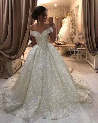 Sparkling Off-the-Shoulder Princess Wedding Dress A bride posing in front of a mirror in a bridal atelier, wearing a stunning, voluminous princess-style wedding gown made of shimmering fabric with an elegant off-the-shoulder neckline.