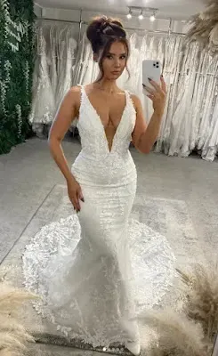 Elegant Plunging Neckline Mermaid Wedding Dress with Floral Lace A bride taking a mirror selfie in a bridal shop, wearing a form-fitting mermaid-style wedding gown featuring a deep plunging neckline, delicate floral lace detailing, and a sweeping train.