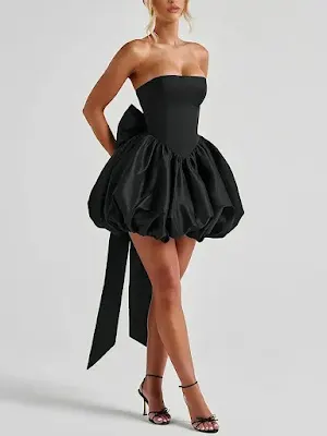 Model wearing a chic black strapless mini dress featuring a voluminous bubble skirt and a large bow on the back, paired with black strappy heels against a neutral background.