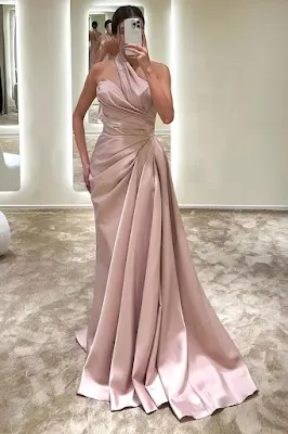 Woman taking a mirror selfie while wearing a long blush pink satin one-shoulder gown with a draped bodice and an elegant train.