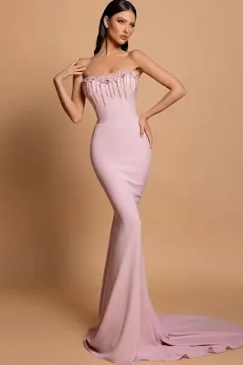 Model posing in a studio wearing a light pink mermaid-style prom dress with a strapless neckline, crystal fringe, and beaded embellishments.